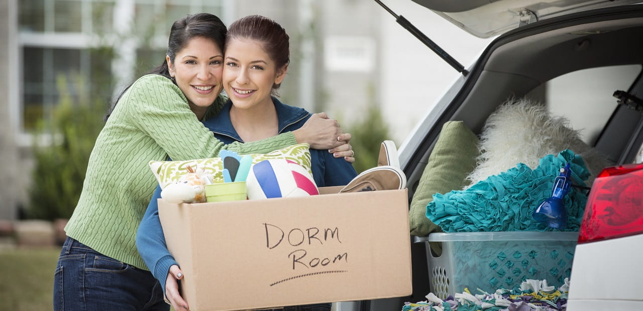 Mother and daughter pose for a photo in front of a car trunk full of college dorm supplies. 