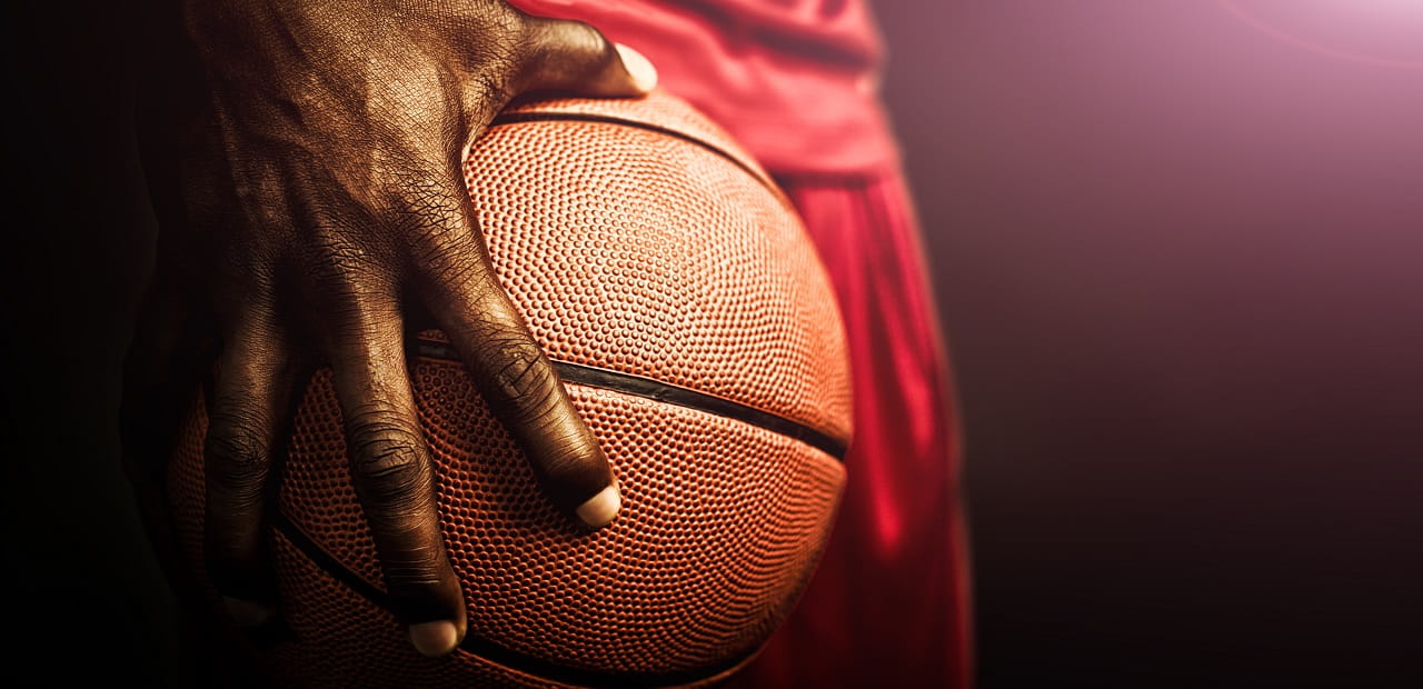 Athlete holds a basketball against his hip with one hand. 