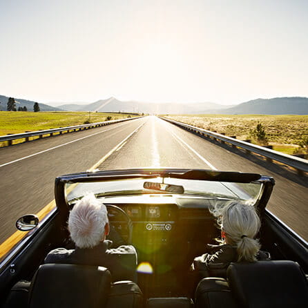 Senior couple driving convertible car at sunrise