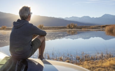 He looks off as the mountain ranges reflect in the lakeshore