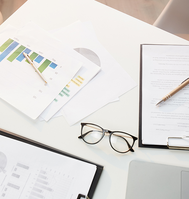 Above view of business documents, pen, eyeglasses on office desk