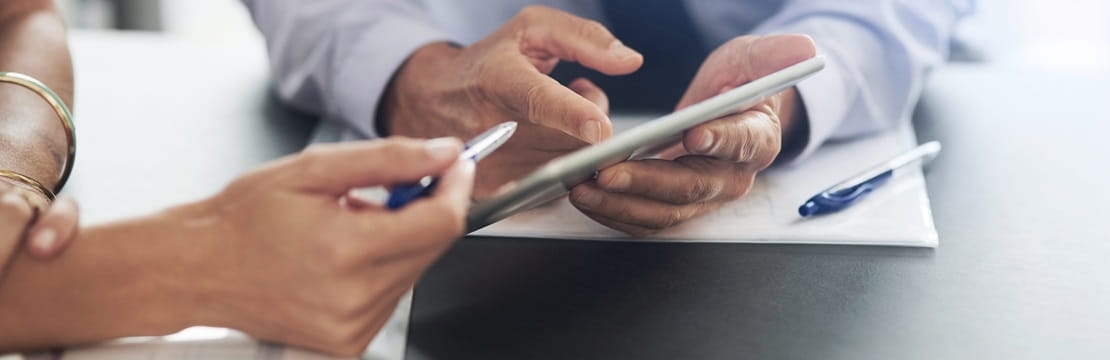 A man's hands pointing to something on a tablet that he's holding and a woman's hand pointing to the tablet with her pen.