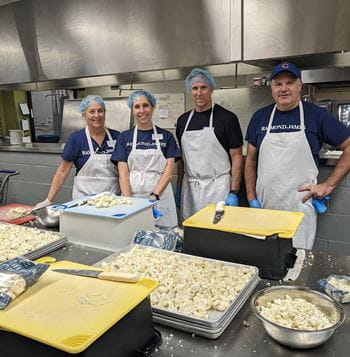 Volunteers wearing aprons and hair nets pose in front of chopped veggies