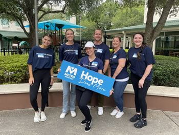 Associates wearing Raymond James Cares shirts hold "Hope does more" Metropolitan Ministries sign